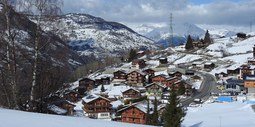 Houses with snow-covered roofs in Grächen and distant snow-covered mountains.