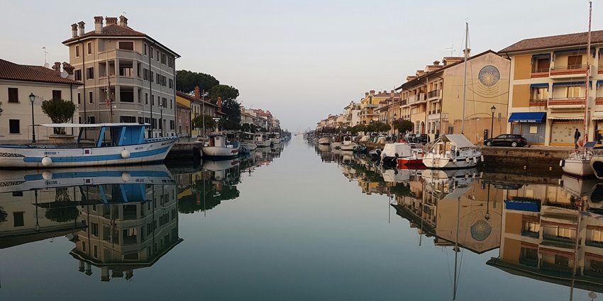 Grado in Italy with a water body of a canal, multiple motorboats parked, and distant buildings.