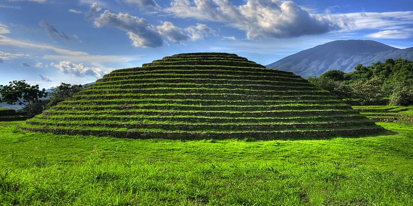 Ancient circular pyramid at Guachimontones, surrounded by grassy hills under open skies.