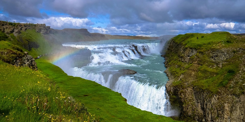 Gullfoss waterfall in Iceland with a two-stage waterfall, a rainbow formation and greenery.