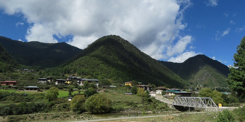 Haa valley with a bridge connecting the town and shaded mountains under a cloud.