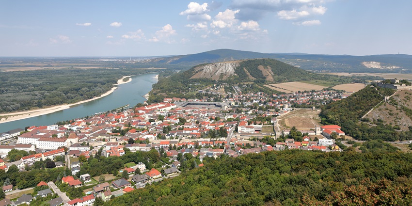 Aerial view of a riverside town with red roofs and hills among places to visit near Bratislava.