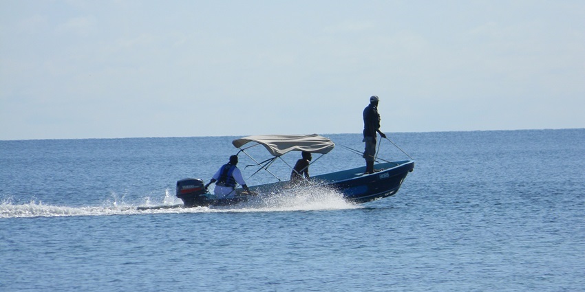 Three people on the boat fishing in calm water and a cloth covering the top of the boat, one of the best things to see in Placencia Belize.