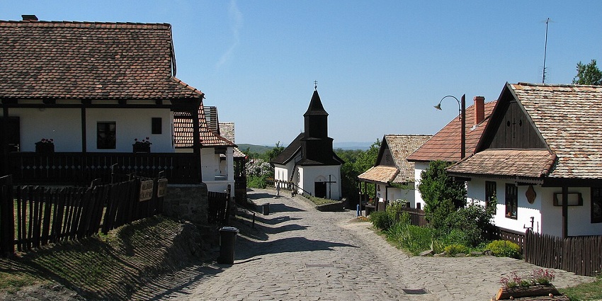 Charming cobblestone street lined with traditional houses and a small wooden church, amongst the places to visit near Budapest.