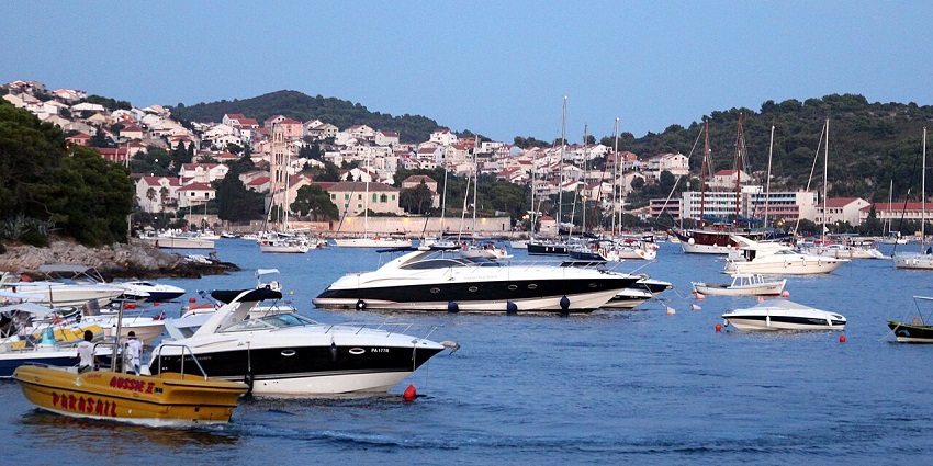 Hvar island with the crowd of white boats, people on the boats, and buildings at a distance.
