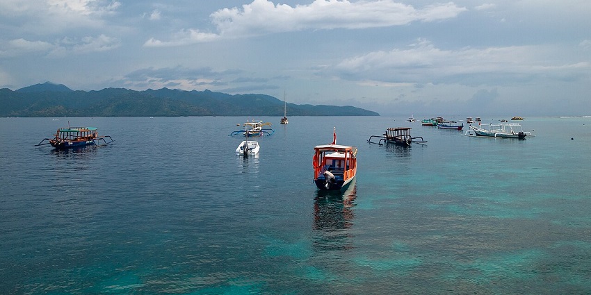 Boats floating on calm waters under cloudy skies near the Gili Islands, among the places to visit near Thailand.
