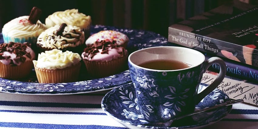 A tea cup with frosted cupcakes on a plate, set on a wooden table with soft lighting.