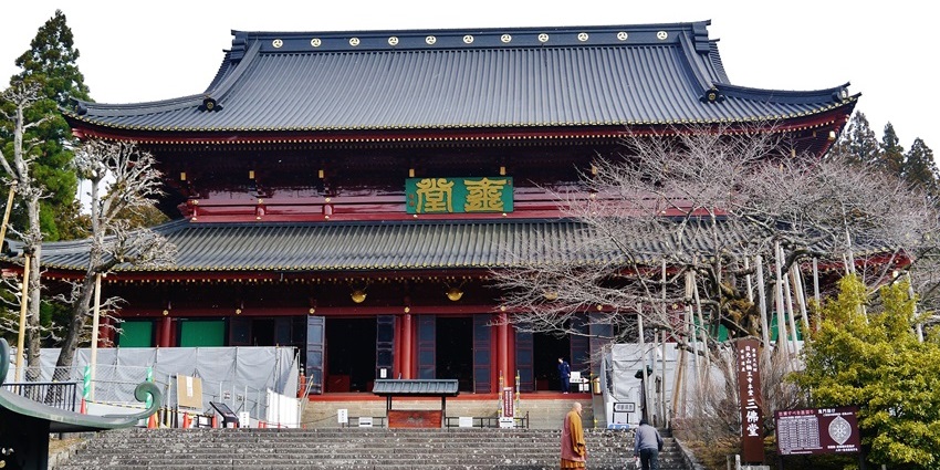 Large traditional wooden temple with ornate roof, stone steps, and people near the entrance.