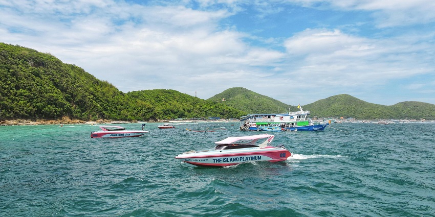 Speedboat cruising through clear blue waters near tropical islands under a sunny sky.