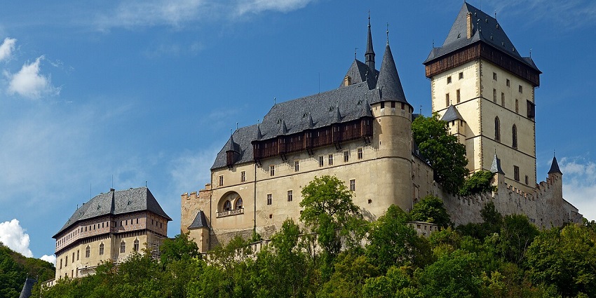 Hilltop vista of Karlštejn Castle with its imposing towers towering above the forest, among places to visit near Prague.