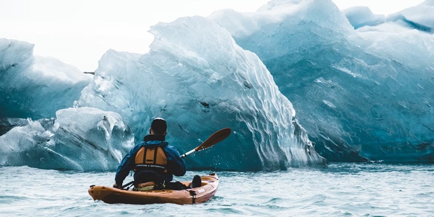 Kayakers paddling through calm waters surrounded by icebergs in a glacier lagoon.