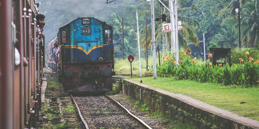 Blue and brown train stationed on tracks with overhead lines and a platform.