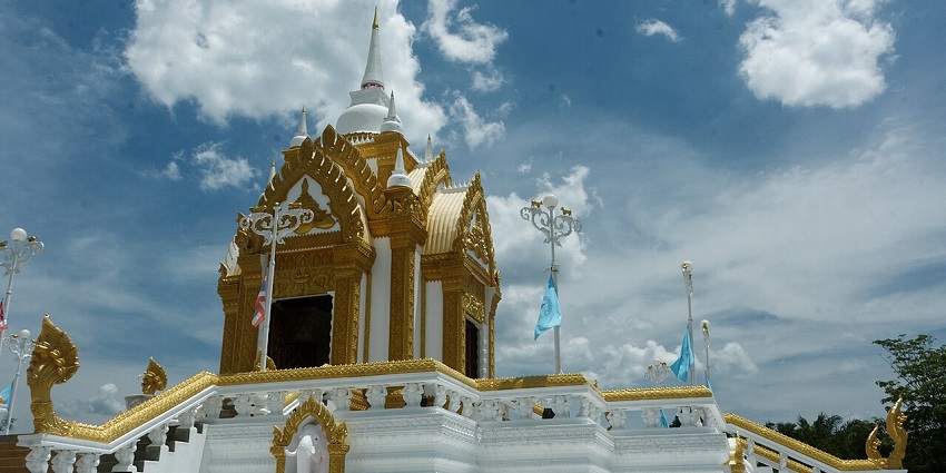 City shrine in Khanom with a white & gold architectural building, multiple flags and pole lightings.