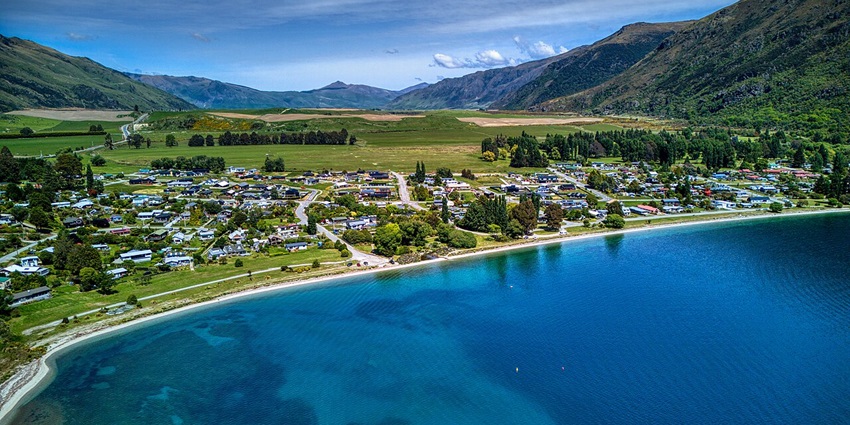 Kingston in a green landscape from above, lining the Lake Wakatipu and surrounded by mountains.