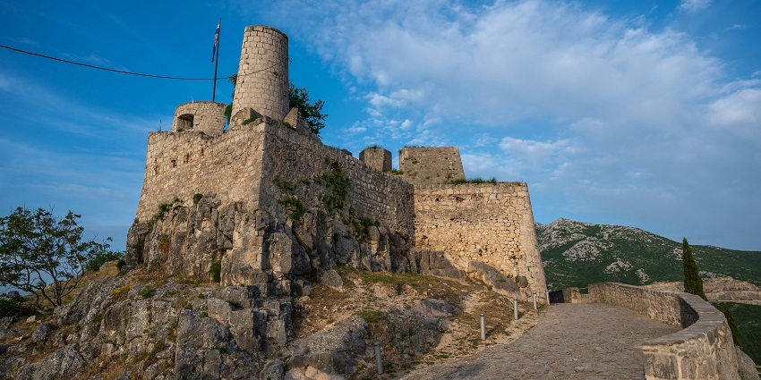 Stone walls and gate of Klis Fortress with city view in the background, amongst the places to visit near Split.
