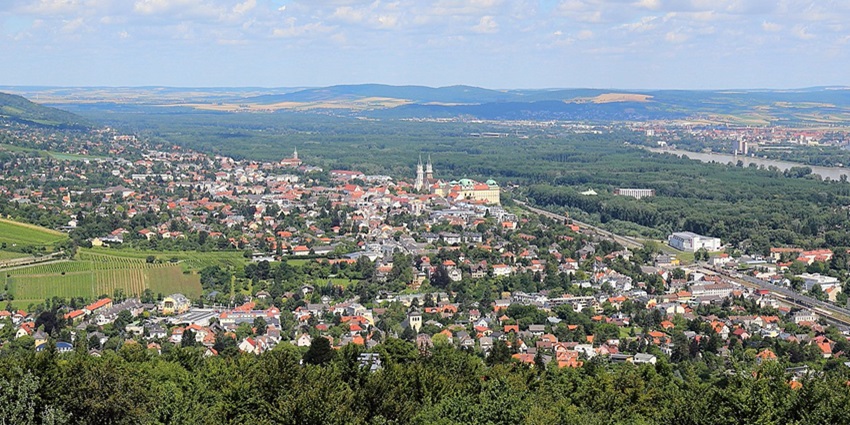 Klosterneuburg from above with distant red roofs of the buildings, the river flowing, and greenery.