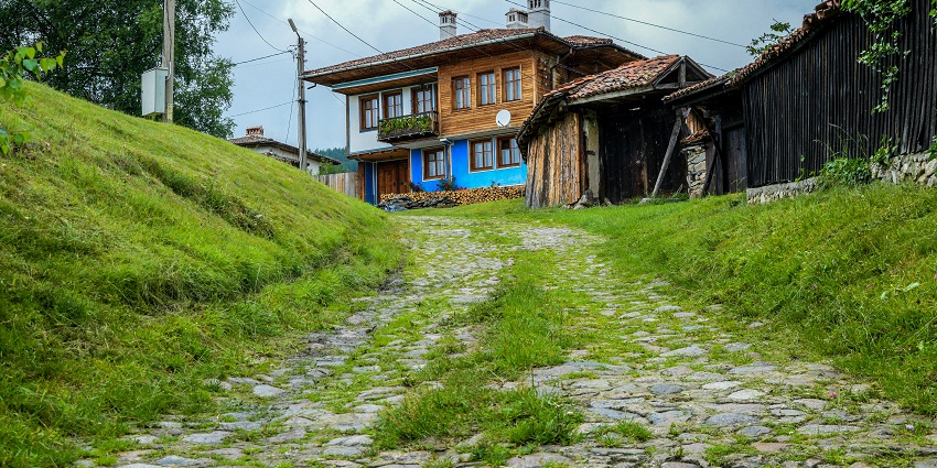 Traditional Bulgarian house on a cobblestone street in Koprivshtitsa with greenery around.