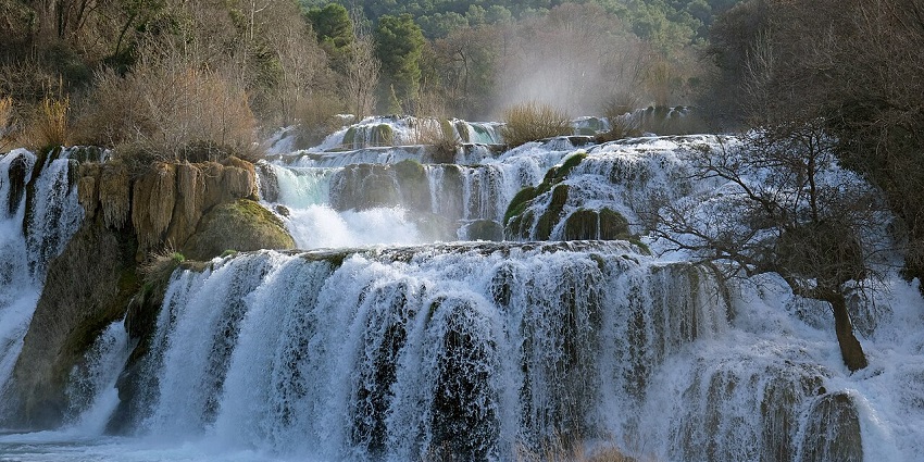 Skradinski Buk waterfalls at Krka National Park with water flowing on an uneven surface and greenery.
