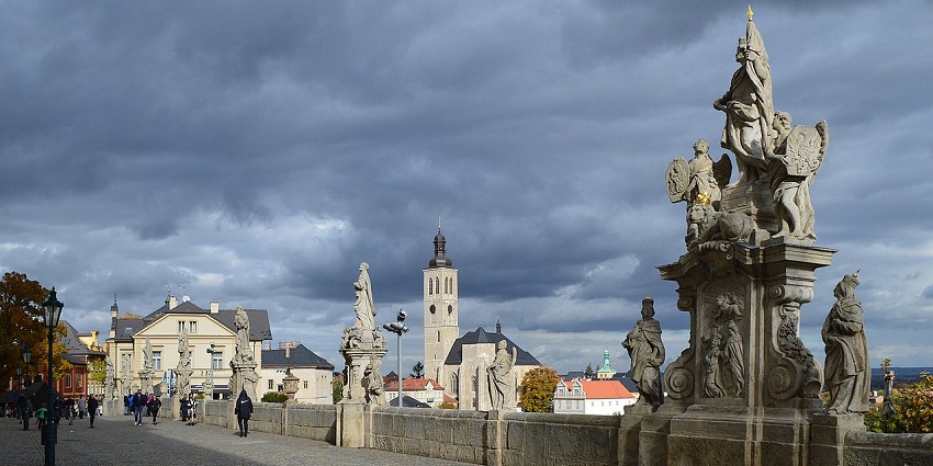 A historic cobblestone walkway lined with baroque statues under a dramatic, cloudy sky.