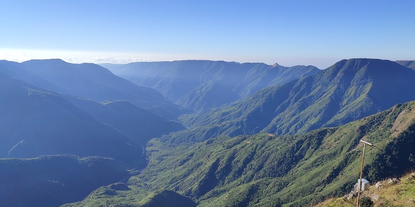 Huge green canyon cliffs at Laitlum, with rolling hills and misty sky in Meghalaya’s serene landscape