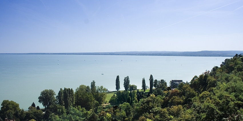 Lake Balaton shoreline with calm waters, waterfront houses, and surrounding hills.