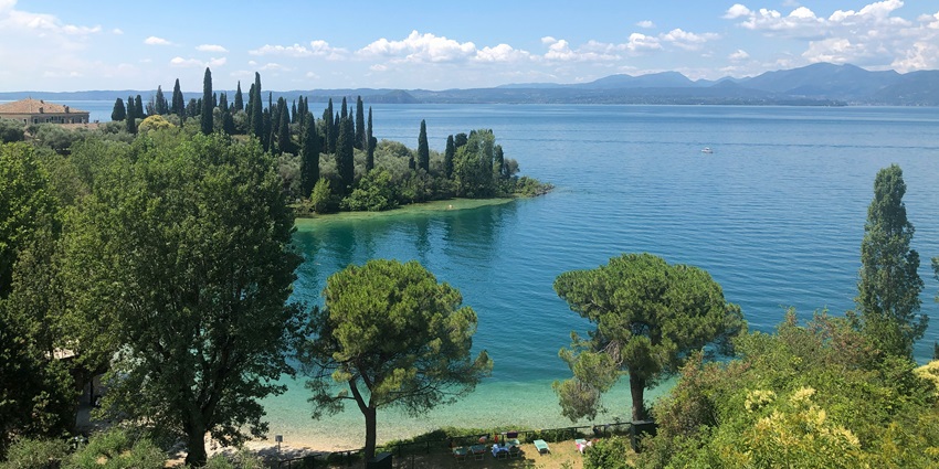 Lake Garda from a distance with a large blue water body, tall green trees, amongst the top places to visit near Venice.