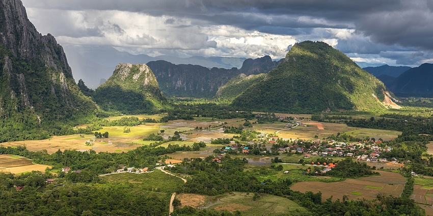 Green Karst mountains and lush rice fields under stormy skies in Vang Vieng, Laos.
