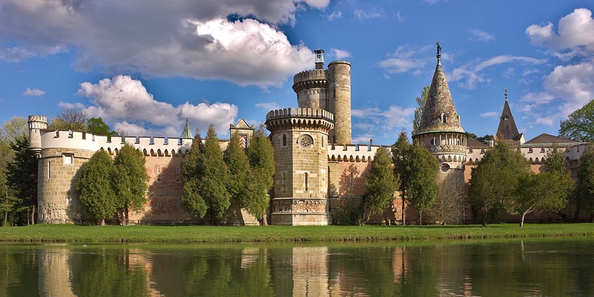 Laxenburg Castle Park with an old Austrian architectural castle, a still water body, and a cloudy sky.