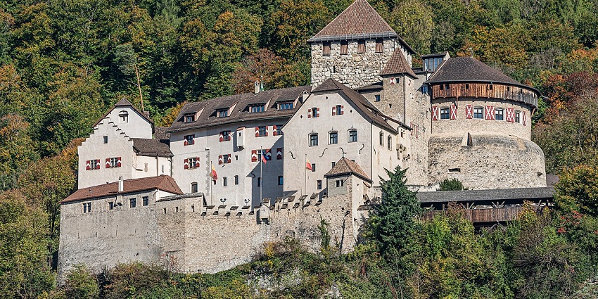 Historic Vaduz Castle on a wooded hilltop surrounded by forest, scenic places to visit near Switzerland.