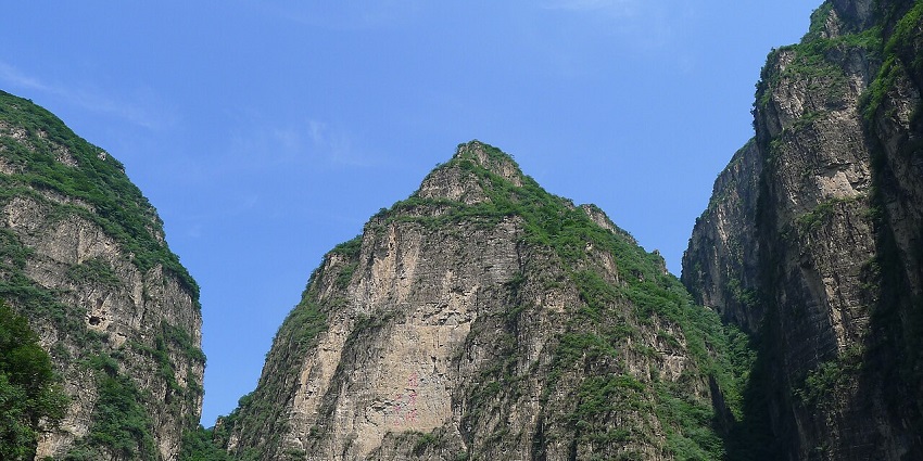 The steep rocky cliffs of Longqing Gorge rise dramatically under clear skies in daylight.
