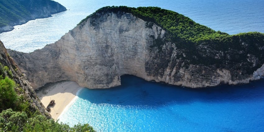 Clear turquoise waters at Psarou Beach with rocky hills and blue skies above.
