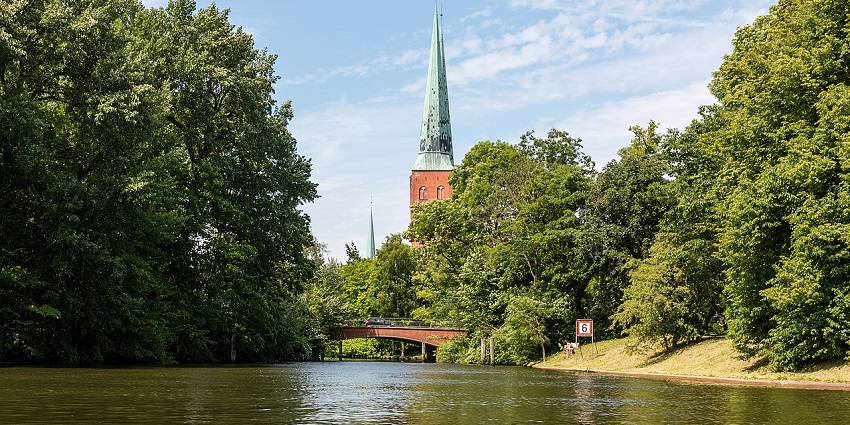A peaceful river scene with a red bridge, lush green trees, and a church spire in view.