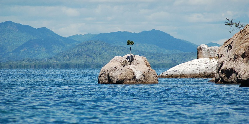 Cape Maclear in Malawi with calm waters, a large stone in midwater, and mountains behind.