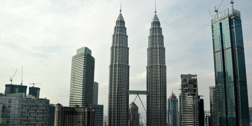 The Petronas Towers rise prominently in the city center, surrounded by smaller buildings.

