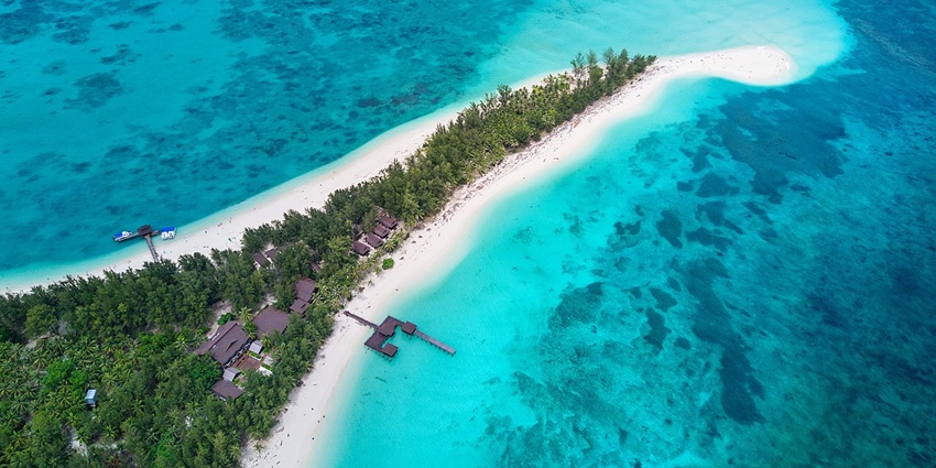 Mantanani Island from above with distant small buildings, sandy shoreline, and boats, amongst the top places to visit near Kota Kinabalu.
