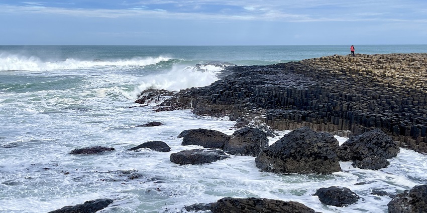 Rocky coastal scene with unique basalt columns and waves crashing against the shore.