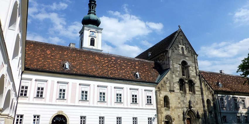 Heiligenkreuz Abbey with historic architecture, red rooftops, and surrounding greenery.