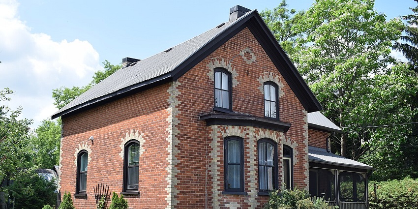 A single historic brick house in Merrickville, Ontario, set amidst lush green surroundings.
