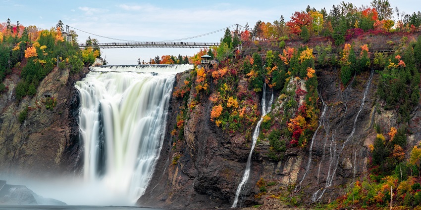 Montmorency Falls flowing into river with autumn trees and bridge in the park.