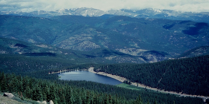 Mountain landscape with pine trees and a calm lake reflecting the surrounding scenery.