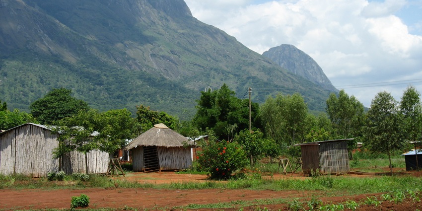 Mulanje Massif in Malawi with rugged peaks, grassy slopes, clouds, and small huts below.
