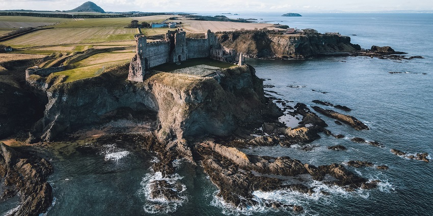 Tantallon Castle ruins overlooking the sea, with lush grass and Bass Rock in view.