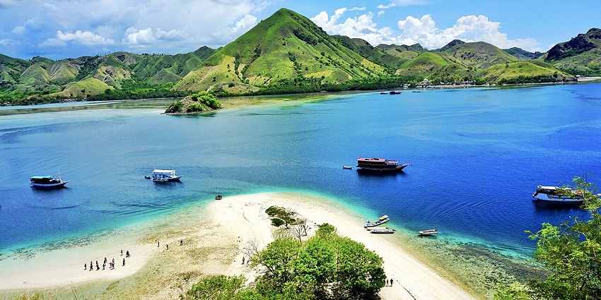 A fishing boat anchored near the shore with a lush, green island in the background under a partly cloudy sky.