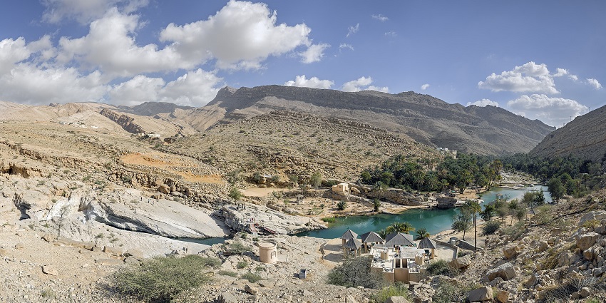 Rocky river gorge with turquoise water pools surrounded by lush green palm trees.