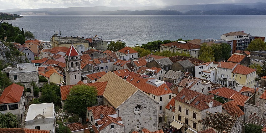 Omiš from above with white buildings & red roofs of houses, buildings, a large water body, and trees.
