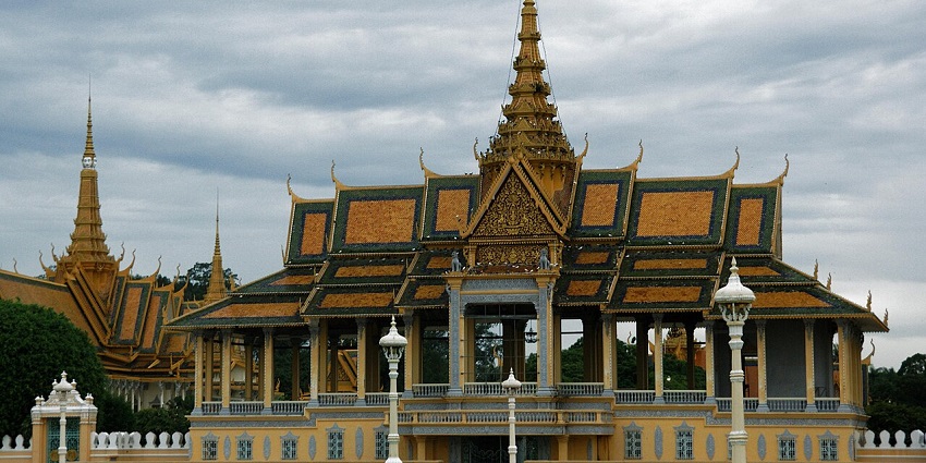 Golden-roofed palace with ornate spires, open sides, and people walking in the front garden.