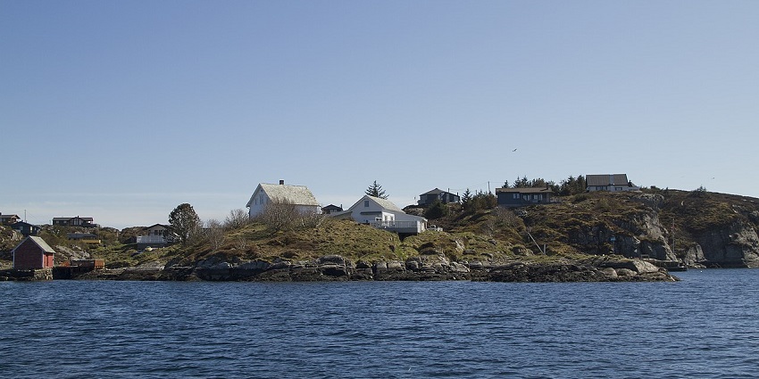 Øygarden in Norway with a blue water body, rocks on the shore and distant houses.