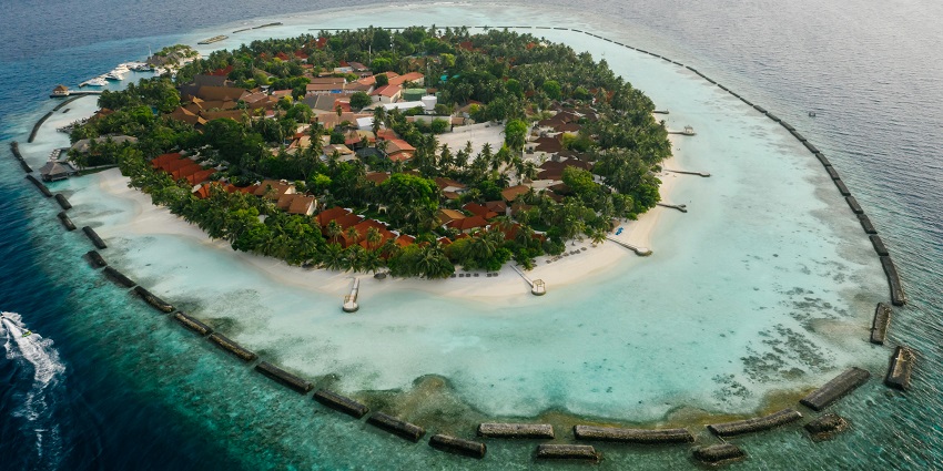 Aerial view of an island with houses, dense greenery, beach, and surrounding water.
