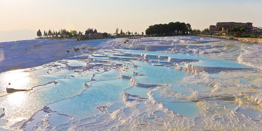 Natural white travertine terraces filled with turquoise thermal water under soft sunlight.