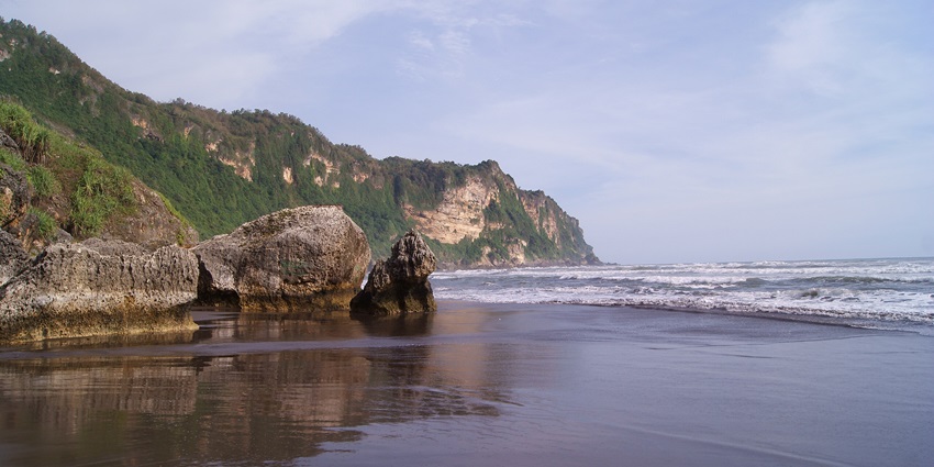 Parangtritis Beach with wide sandy shores, crashing waves, and a dramatic coastal backdrop.